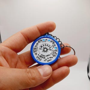 May include: A blue and white circular keychain with the text "SMASHPAD" and "TAP-O-WAR GAMES". The keychain has a silver chain and a key ring. The design includes a score zone and various game-related indicators.
