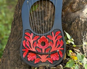 Lira negra de 10 cuerdas con diseño de hojas y flores rojas. Incluye llave de afinación, funda y juego de cuerdas.