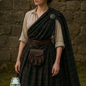 Puede incluir: Una mujer con un atuendo tradicional escocés. El conjunto incluye un kilt a cuadros verde y marino, un chal a juego, un cinturón de cuero marrón y un pequeño sporran de cuero. Un broche plateado asegura el chal.
