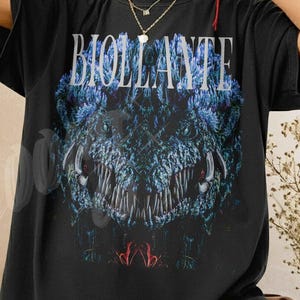 May include: Black t-shirt with the word "BIOLLANTE" in white block letters above a blue and black monster graphic. The shirt has short sleeves and a relaxed fit. The text "Shirt Color Black" is at the bottom left.