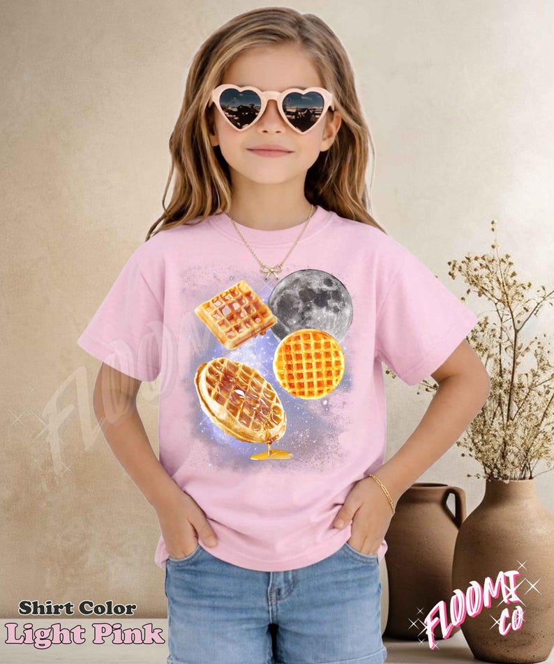 May include: Light pink t-shirt featuring a waffle and moon graphic. The shirt has a crew neck and short sleeves. The text "Shirt Color Light Pink" is at the bottom left of the image.