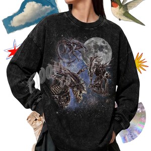 May include: A black long-sleeve tee with a mineral wash finish. The front features a graphic of three extraterrestrial creatures against a starry space background with a large moon. Text at the top reads Premium Long Sleeve Tee Color Black.