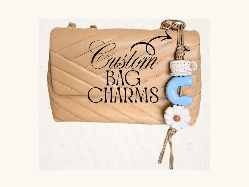 May include: A beige quilted handbag with a decorative bag charm. The charm includes a blue letter "C", a white daisy, and a small teacup. The text "Custom BAG CHARMS" is written on the bag.