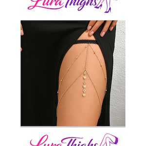 May include: A gold-coloured body chain with a delicate design. The chain features small beads and decorative charms, including butterfly shapes. The text "Lura Thighs" is displayed in a stylized font.