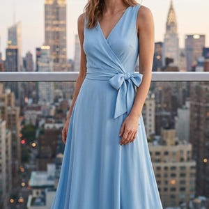May include: A sleeveless light blue floor-length dress featuring a V-neckline, a wrap-style bodice, and a fabric tie at the waist that forms a bow on the left side. The dress has a fitted waist and a long, flowing skirt that reaches the ground.