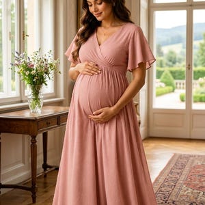 May include: A floor-length dusty rose maternity dress featuring a V-neckline, short flutter sleeves, and a wrap-style bodice. The fabric has a subtle textured dot pattern throughout, with a flowing skirt that drapes to the floor.
