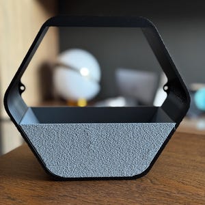 Peut inclure: Une étagère murale hexagonale noire avec un intérieur gris texturé. L'étagère a un design moderne et est faite d'un matériau robuste. L'étagère est vide et prête à être remplie d'objets décoratifs.