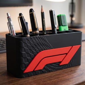 Peut inclure: Organisateur de bureau noir avec le logo Formula 1 rouge. Il contient des stylos, des crayons et un surligneur. Le côté de l'organisateur présente un motif en losanges texturé.