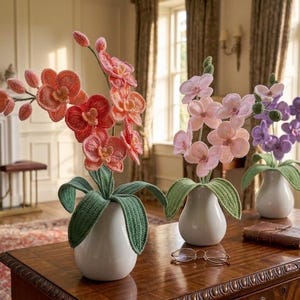 May include: Three decorative orchid arrangements in white vases on a wooden table. The orchids are in shades of pink, orange, and purple, with green leaves. A candle and a book are also on the table. The room has a classic, elegant style.