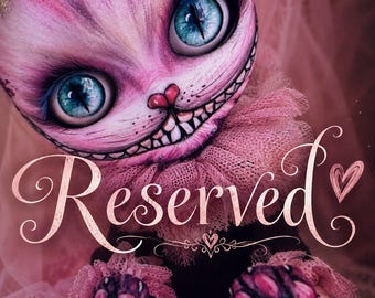 May include: A doll with a pink feline face, large blue eyes, and a wide grin showing teeth. It wears a pink ruffled collar and has dark paws with pink pads. The word Reserved is written in elegant script across the center with a small heart.