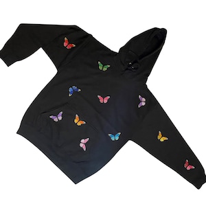 May include: Black hoodie with a colorful butterfly pattern. The hoodie has a drawstring hood and a kangaroo pocket.