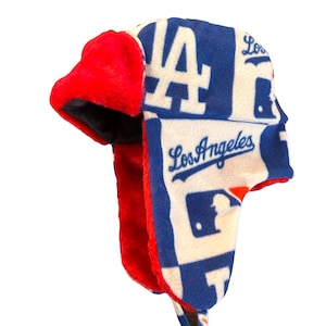May include: A blue and white fleece trapper hat with a red faux fur ear flap. The hat features the Los Angeles Dodgers logo and the team's name.