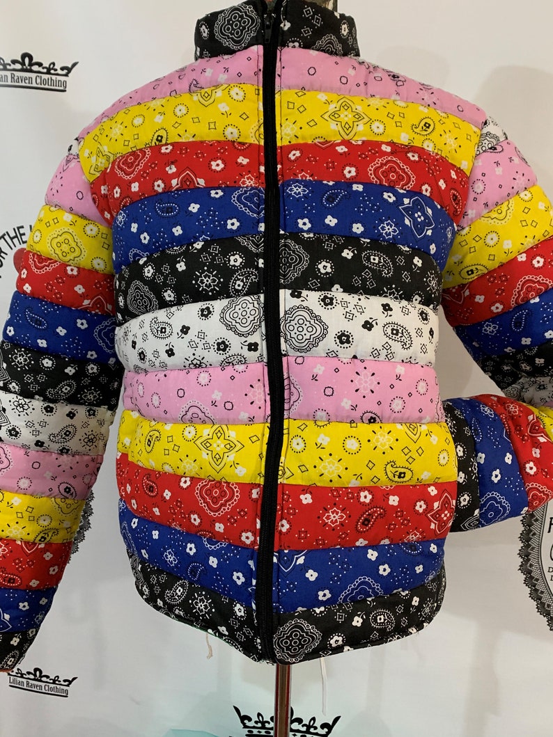 May include: A colorful puffer jacket with a black zipper and a bandana print. The jacket has stripes of pink, yellow, red, blue, and black.