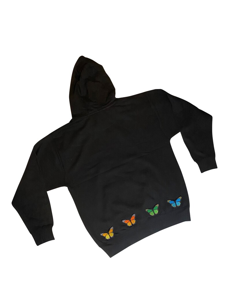 May include: Black hooded sweatshirt with four embroidered butterflies in rainbow colors on the bottom hem.
