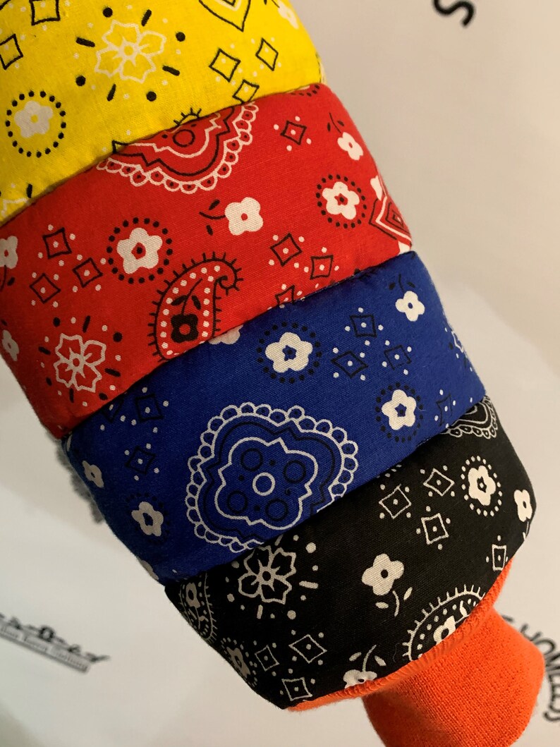 May include: A stack of four bandanas in different colors, yellow, red, blue, and black, with a white paisley pattern. The bandanas are folded and stacked on top of each other.