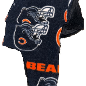 May include: Navy blue trapper hat with orange and white accents. The hat features the word "BEARS" in orange and white football helmet graphics. The ear flaps are lined with black faux fur.