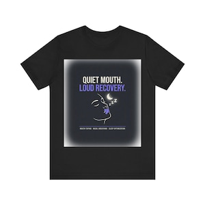 May include: A black short-sleeve t-shirt featuring a graphic with the text QUIET MOUTH. LOUD RECOVERY. and MOUTH TAPING - NASAL BREATHING - SLEEP OPTIMIZATION. The design includes a white line drawing of a face with a purple piece of tape over the mouth.