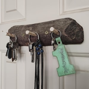 May include: A wooden key holder with three pegs, each holding a set of keys. The wood is a natural brown colour, and the keys hang from metal rings. One key has a green tag with the number 1 and the word "presscode".