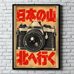 May include: A framed poster featuring a vintage-style 35mm film camera centered on a tan background. The image includes bold red Japanese text above and below the camera. The camera has a black textured body with silver metallic accents.