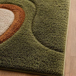 May include: A rectangular area rug featuring a high-pile, shaggy texture with a geometric pattern of concentric semi-circles. The design incorporates shades of olive green, burnt orange, and cream, creating a layered, textured visual effect.