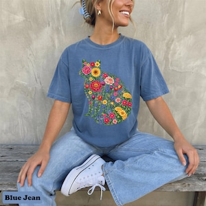 May include: Blue jean colored t-shirt featuring a floral cat design. The cat silhouette is filled with colorful flowers, including pink roses, yellow sunflowers, and red tulips. The text "Blue Jean" is at the bottom.