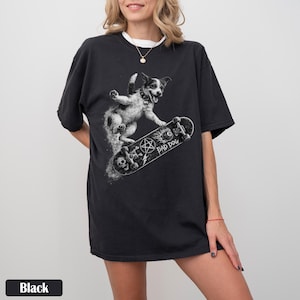 May include: Black t-shirt featuring a graphic of a dog on a skateboard with the text "BAD DOG". The dog is black and white, and the skateboard has a skull and pentagram design. The shirt has a relaxed fit.