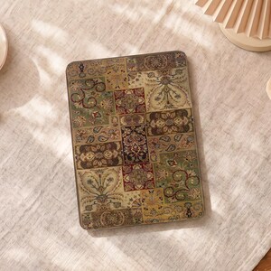 May include: A rectangular electronic e-reader device featuring a protective cover with a multi-colored patchwork design. The pattern consists of various intricate floral and paisley motifs in shades of deep red, olive green, gold, and brown.