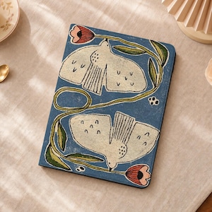 Peut inclure: Une housse de tablette rectangulaire avec un fond bleu, deux oiseaux blancs en vol, des tiges vertes et des fleurs roses en forme de tulipes. Le motif présente un aspect brodé et texturé qui recouvre toute la surface avant de l'étui.