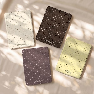May include: Four rectangular e-reader cases featuring a polka dot pattern. The cases are cream, dark brown, light purple, and pale yellow. Each case is personalized with a name printed in a serif font: Brooklyn, Vanessa, Shirley, and Olivia.