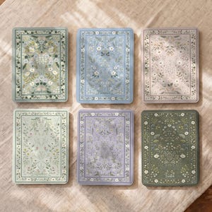 May include: Six rectangular notebooks with floral patterns in shades of sage green, light blue, soft pink, pale green, lavender, and dark olive. Each cover features a botanical illustration and a personalized name printed at the bottom center.