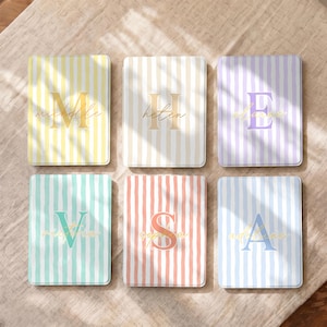May include: Six rectangular items featuring vertical stripes in yellow, beige, lavender, mint green, coral, and light blue. Each item displays a large serif capital letter in the centre with a cursive name printed over it: Michelle, Helen, Elanne, Victoria, Sophia, and Adeline.