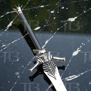 May include: A decorative sword with a skull-shaped hilt and a long, polished blade. The hilt is silver with a detailed skull design and cross-shaped handguards. The blade is silver and reflects light. The sword is black and silver.