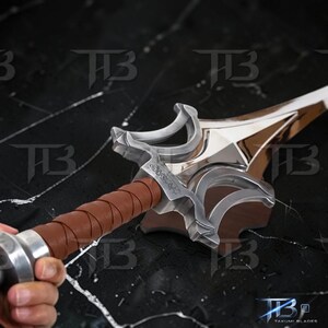 May include: A close-up of a sword with a shiny silver blade and a brown leather-wrapped handle. The hilt has ornate silver detailing. The sword is held, highlighting the craftsmanship and design of the weapon.