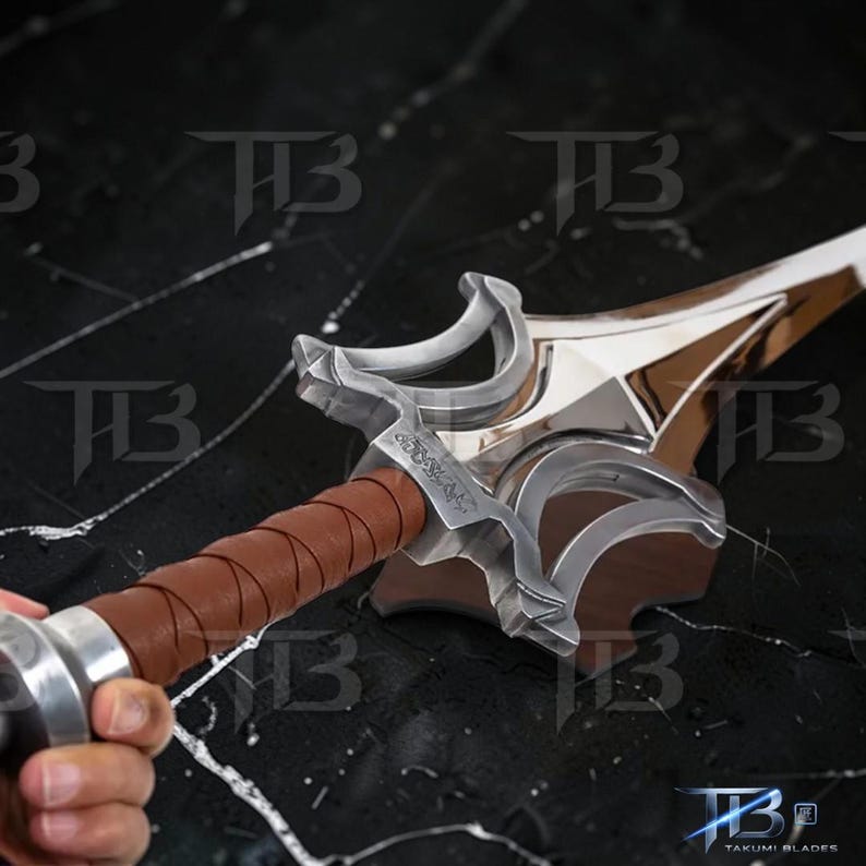 May include: A close-up of a sword with a shiny silver blade and a brown leather-wrapped handle. The hilt has ornate silver detailing. The sword is held, highlighting the craftsmanship and design of the weapon.