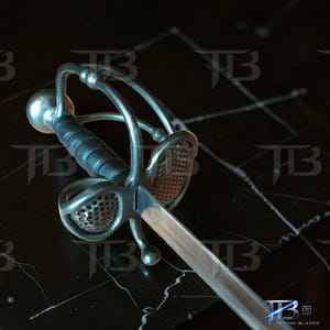 Könnte beinhalten: Nahaufnahme eines Rapier-Schwerts mit silberner Klinge und aufwendiger Metallarbeit. Der Griff ist mit schwarzem Leder umwickelt. Das Schwert hat einen komplexen Parier. Der Hintergrund ist dunkel und strukturiert.