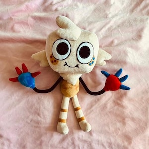 May include: A plush toy character with a cream-colored head, large black eyes, and small wings. The toy has black arms ending in red and blue hands. The body is tan and white, with tan and orange striped legs.