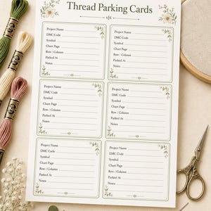 May include: A white paper sheet titled Thread Parking Cards with six rectangular sections for embroidery organization. Each section includes lines for project name, DMC code, symbol, chart page, row, column, parked at, and notes, decorated with green floral accents.