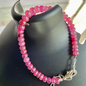 Könnte beinhalten: Ein Armband aus kleinen, runden, durchscheinenden rosa Perlen. Das Armband verfügt über einen silberfarbenen Karabinerverschluss aus Metall und eine verstellbare Kettengliederverlängerung an einem Ende, die den kreisförmigen Strang aus polierten Steinen sichert.