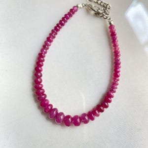 Puede incluir: Una pulsera compuesta por pequeñas cuentas de piedras preciosas facetadas de color rosa intenso dispuestas en una sola hebra. La pulsera cuenta con un cierre de mosquetón de metal plateado y una cadena de extensión ajustable.