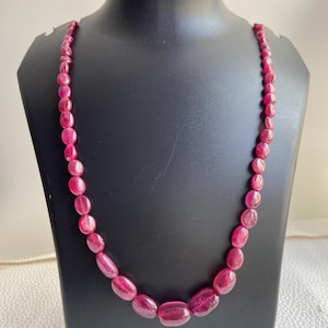 Peut inclure: Un collier composé de nombreuses perles polies de forme ovale dans une teinte magenta-rose profond. Les perles sont enfilées ensemble en un seul brin, la taille des perles augmentant progressivement vers le centre du collier.