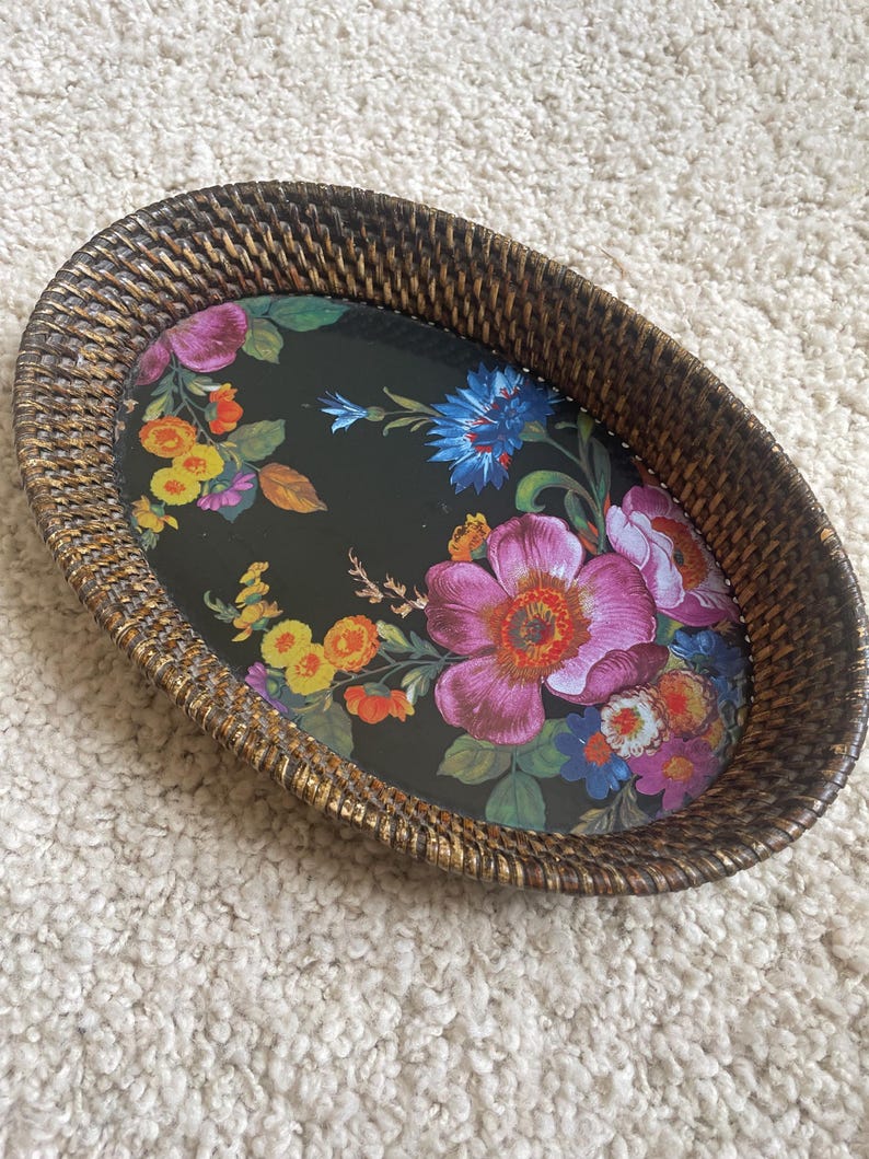 Puede incluir: Una bandeja ovalada con un borde de rat&aacute;n trenzado de color marr&oacute;n oscuro y una base negra con un estampado floral colorido. El dise&ntilde;o incluye grandes flores rosas, naranjas, amarillas y azules con hojas verdes sobre la superficie oscura.