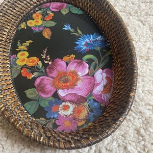 Puede incluir: Una bandeja de forma ovalada con un borde de rat&aacute;n tejido en color marr&oacute;n oscuro y una base plana decorada con un estampado floral vibrante sobre un fondo negro. El dise&ntilde;o floral incluye grandes flores rosas, azules, amarillas y naranjas.