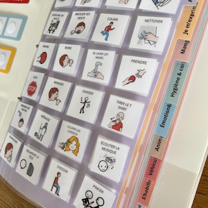 Peut inclure: Un classeur de communication composé d'une grille de cartes carrées avec du texte français et des illustrations simples représentant des actions quotidiennes comme dormir, courir et manger. Le classeur comporte des onglets colorés étiquetés Action, Je m'exprime, Manger, Hygiène & corps, Émotion, Animaux, Véhicules, S'habiller et Jeu/activité.