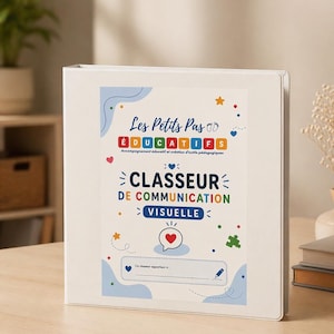 Peut inclure: Un classeur blanc avec des inscriptions colorées. On peut lire "Les Petits Pas ÉDUCATIFS" et "CLASSEUR DE COMMUNICATION VISUELLE". Des cœurs, des étoiles et des pièces de puzzle décorent le classeur. Il est posé sur une surface en bois clair.
