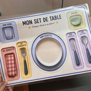 Peut inclure: Un set de table pour enfants avec des illustrations d'un verre, d'un bol, d'une assiette, d'un couteau, d'une cuillère, d'une fourchette et d'une serviette. Le texte "MON SET DE TABLE" et "Chaque chose à sa place!" sont également visibles.