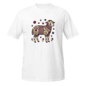 May include: White t-shirt featuring a colorful, patterned illustration of a sheep. The sheep design incorporates floral and geometric elements in shades of red, blue, yellow, and green. Surrounding the sheep are small floral accents.