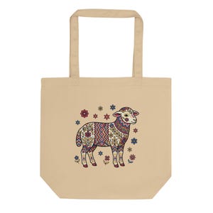 May include: Beige tote bag featuring a colorful, patterned illustration of a sheep. The sheep design incorporates floral and geometric elements in shades of red, blue, and cream. The bag has a simple, rectangular shape with two handles.