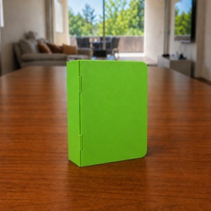 Puede incluir: Un estuche rectangular de color verde lima brillante con un acabado mate suave y una bisagra vertical en el lado izquierdo. El objeto se mantiene en posici&oacute;n vertical, con un exterior liso y s&oacute;lido, esquinas redondeadas y un dise&ntilde;o funcional.