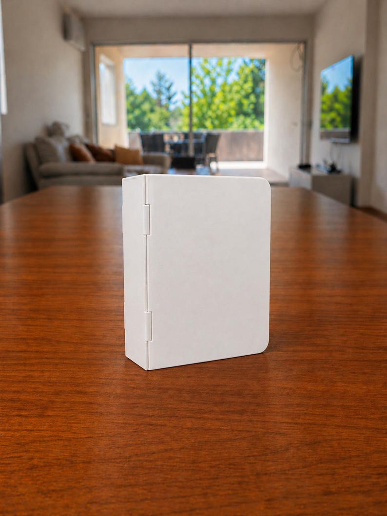 Puede incluir: Una carpeta rectangular de color blanco s&oacute;lido con un acabado mate suave y una bisagra vertical en el lado izquierdo. El objeto se mantiene en posici&oacute;n vertical sobre su borde, con un dise&ntilde;o limpio y esquinas redondeadas en el lado derecho.