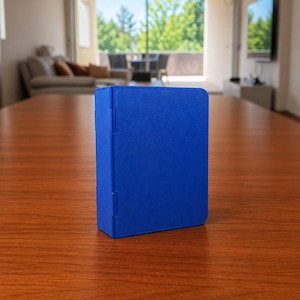 Puede incluir: Una caja de almacenamiento rectangular de color azul s&oacute;lido con un acabado mate suave y un panel lateral con bisagras. El objeto se mantiene en posici&oacute;n vertical sobre su base, con un color uniforme y un dise&ntilde;o funcional con bisagras visibles.